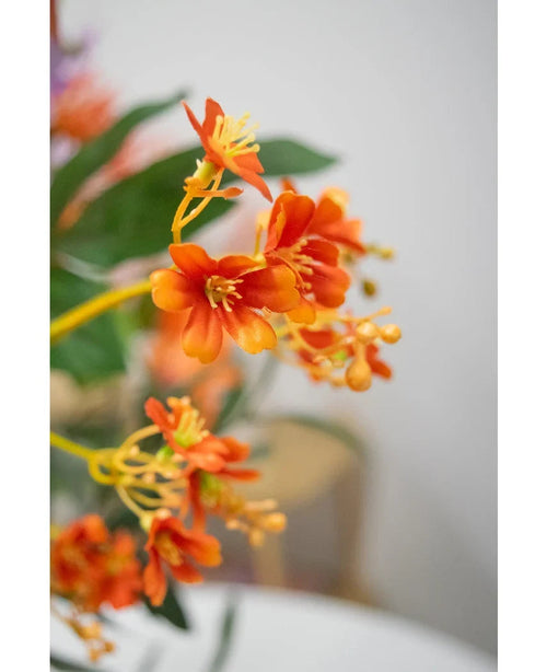 Nærbillede af den 108 cm kunstige gren Daphne Spray i levende orange, med realistiske grønne blade og gule støvdragere, mod en blødt falmet baggrund.