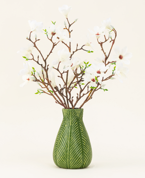 En grøn vase viser Silk kunstig blomsterbuket Magnolia hvid, med flere hvide magnoliagrene med små grønne blade, mod en almindelig lys baggrund.