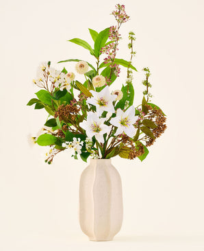 Silke kunstig blomsterbuket Timeless Bloom, bestående af en buket af forskellige hvide liljer, små hvide blomster og grønt i en beige vase med struktur.