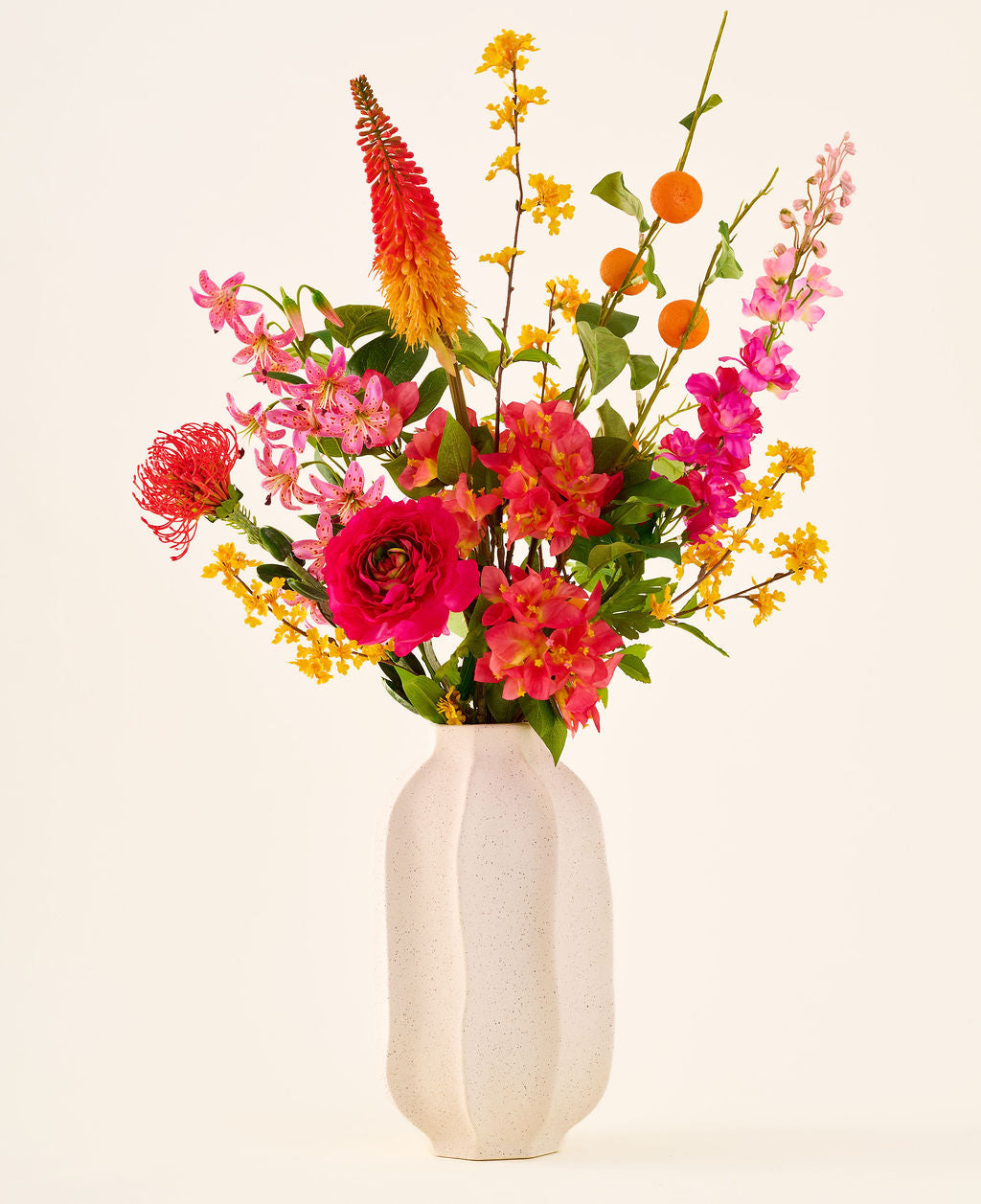 I en hvid keramikvase er 'Summer Blush'-buketten af kunstige silkeblomster, bestående af lyserøde, gule og orange blomster med grønne blade, mod en almindelig lys baggrund.