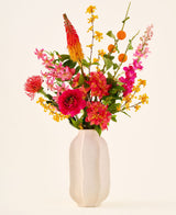 I en hvid keramikvase er 'Summer Blush'-buketten af kunstige silkeblomster, bestående af lyserøde, gule og orange blomster med grønne blade, mod en almindelig lys baggrund.