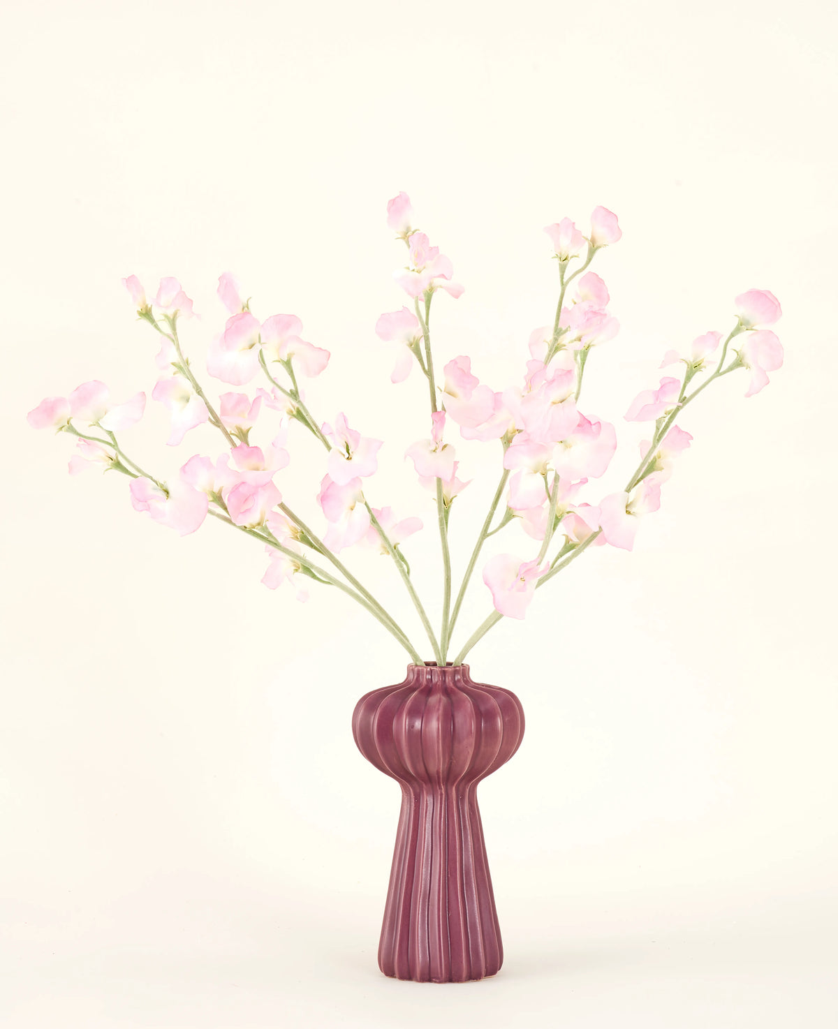 Silk kunstige blomsterbuketten Pea light pink, med flere lys pink ærtestilke i en ribbet bordeaux vase, står på en bleg baggrund - ideel til ethvert kunstigt blomsterinteriør.