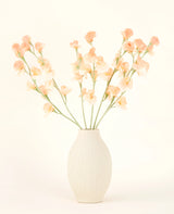 Den cremefarvede keramikvase indeholder Silk kunstig blomsterbuket Pea Peach, med sart fersken og lyserøde blomster med lange grønne stilke mod en lys, neutral baggrund.