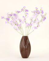 En tekstureret brun vase holder den kunstige silkeblomstbuket Ært lilla-lyse lilla silkeblomster med grønlige stilke mod en almindelig, lys baggrund.