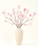 Silke kunstige blomsterbuketten Cherry blossom pink 114 cm har lange, tynde grene med bundter af lyserøde blomster i en beige keramikvase, som danner en slående kontrast mod den almindelige hvide baggrund.