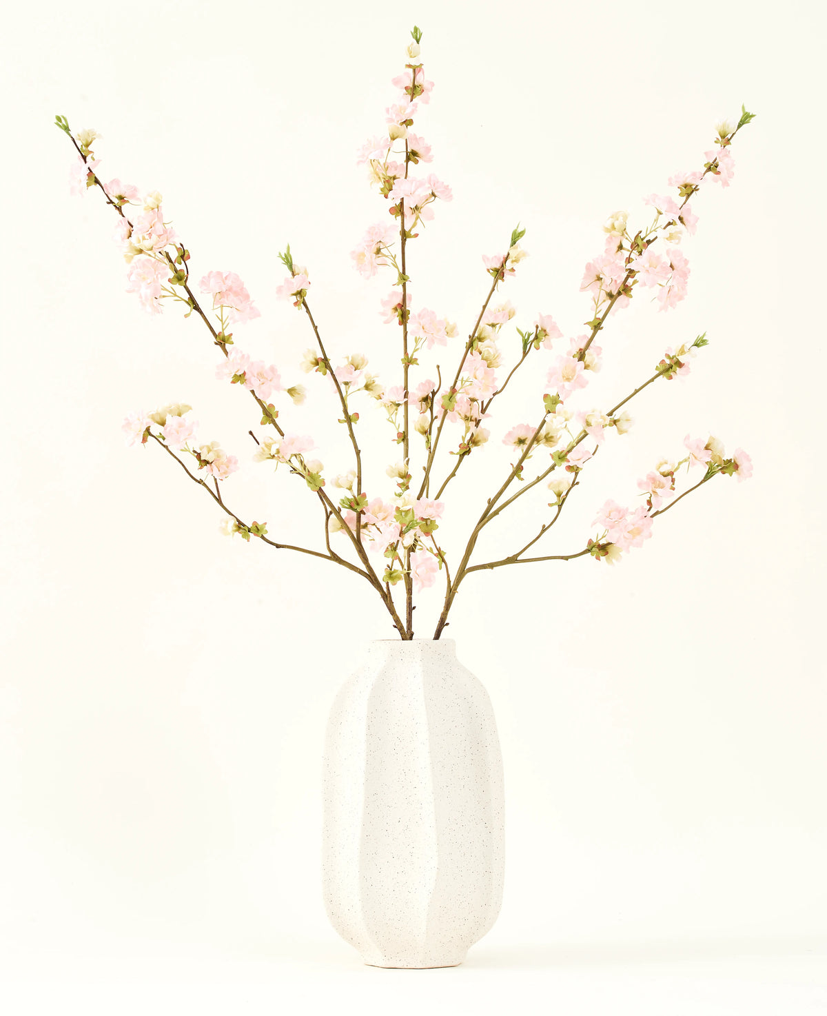 Silke kunstige blomsterbuketten Cherry blossom lys pink 94 cm har sarte pink kunstige kirsebær blomster i en hvid keramik vase, som tilføjer elegance mod en almindelig lys baggrund.