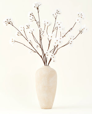 Silke kunstige blomsterbuketten Kirsebærblomstcreme 114 cm står højt i en beige keramikvase og bringer en fredfyldt dekoration til ethvert rum med sine sarte, cremefarvede grene mod en lys baggrund.