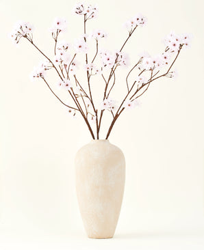 Silke kunstige blomsterbuketten Cherry blossom lys pink 114 cm står i en høj beige keramik vase med lange, tynde grene og sarte lys pink blomster, hvilket skaber en fredfyldt kunstig blomsteraccent mod en almindelig baggrund.