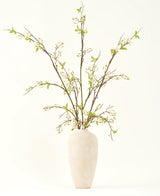 En høj, cremefarvet keramikvase indeholder Silke kunstige blomsterbuket Verbena creme med lange grene, små grønne blade og sarte hvide blomster, smukt arrangeret mod en almindelig lys baggrund.
