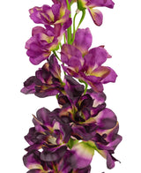 Et nærbillede af Artificial Flower Delphinium Purple 79 cm, en høj kunstig stilk med flere lilla og mørkelilla blomster med et grønt og gult hjerte, mod en hvid baggrund.