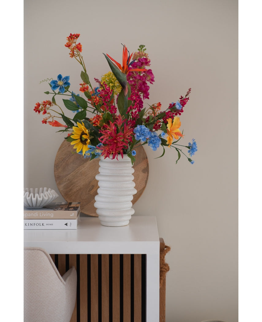En hvid tekstureret vase rummer en 75 cm lyserød buket Artificial Flower Catnip på et hvidt bord ved siden af stablede bøger og indretning, med en rund træbakke lænet op ad den beige væg i baggrunden.