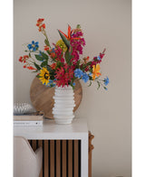 En hvid tekstureret vase rummer en 75 cm lyserød buket Artificial Flower Catnip på et hvidt bord ved siden af stablede bøger og indretning, med en rund træbakke lænet op ad den beige væg i baggrunden.