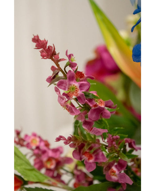 Nærbillede af Artificial Flower Catnip 75 cm pink: en klynge af lyse lyserøde kunstige blomster med et grønt hjerte og frodige blade, skarpt afbildet mod en blødt sløret baggrund med antydninger af andre blomster.