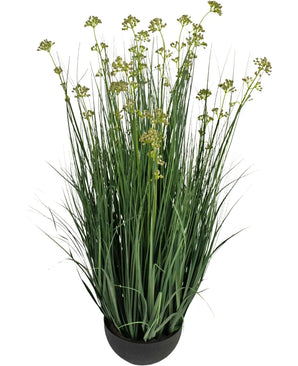 Kunstgræs Porre Blomster Løg Græspotte 100 cm brandhæmmende middel har lange, slanke grønne græslignende blade og små gulgrønne blomsterklaser i en rund sort potte, mod en hvid baggrund.