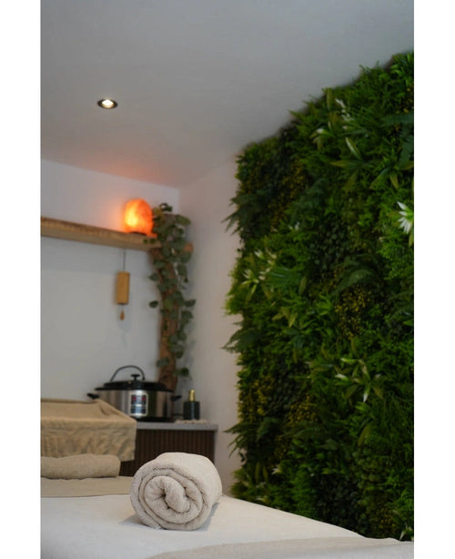 Et roligt spa-område med massagebriks, beroligende belysning, en Himalaya-saltlampe på en hylde og en frodig Artificial Hedge Freshness 100x100 cm UV-grøn plantevæg for ekstra ro.