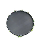 En kunstig hæk på sort stel Ø100 cm trampolin, set fra oven med grønne blade og lyserøde blomster rundt i kanten, mod hvid baggrund.