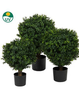 Den kunstige buksbom på stængel UV 40 cm har tre kunstige topiary træer med tæt grønt løv i sorte potter, som er placeret sammen. Et lille UV-symbol med et solikon i øverste venstre hjørne indikerer, at de er UV-bestandige.