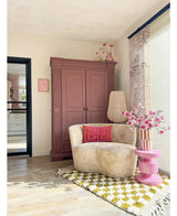 En hyggelig læsekrog har en cremefarvet stol, lyserøde puder, et gult mønstret tæppe og en lilla garderobe. The Artificial Branch Magnolia lilleblomstret 89 cm pink står på et pink sidebord, mens store vinduer fylder dette indbydende rum med blødt lys.