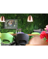 En moderne spiseplads med grønne og ferskenfarvede stole, et bord dekoreret med vaser med lilla blomster, kobberhængende lamper, en frodig plantevæg lavet med Kunsthaag Crush UV-panelet på 100 x 100 cm, og et indrammet billede af en tiger i baggrunden.