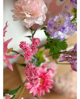 Et nærbillede af Artificial Branch Statice 64 cm pink, med sarte lyserøde statice blomster og grønne blade, arrangeret i en buket mod en blødt falmet indendørs baggrund.