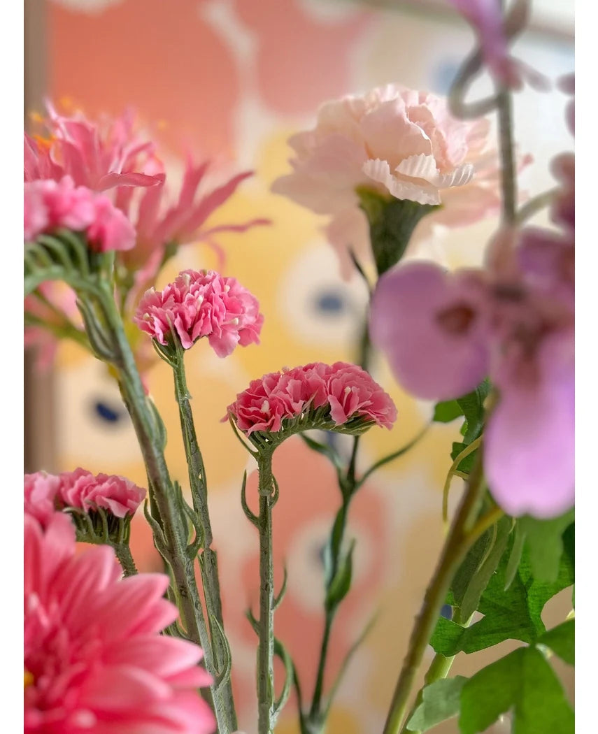 Et nærbillede af Artificial Statice 64 cm lyserøde kunstige blomster, med sarte lyserøde statice blomster mod en sløret pastel baggrund med abstrakte gule og ferskenfarvede former.