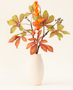 Het Zijden kunstbloemen boeket Herfst Flair heeft een vaas met witte structuur en lampiontak, oranje lampionvormige bloemen en groenrode bladeren, die een stijlvolle herfsttentoonstelling vormen tegen een effen lichte achtergrond.
