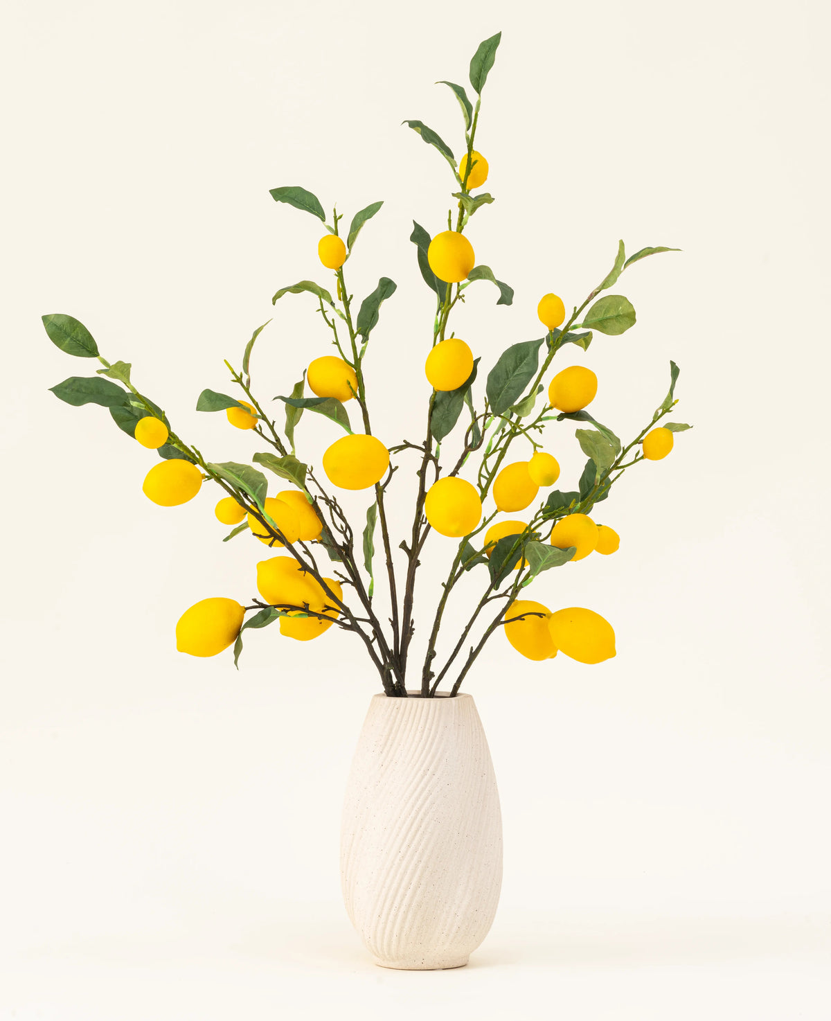 En hvid tekstureret vase viser Lemons kunstige blomsterbuket med grønne blade og levende gule citroner mod en lys baggrund.