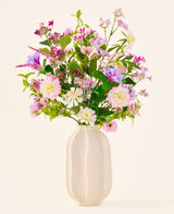 En hvid keramikvase rummer en farverig buket af lyserøde, lilla og hvide blomster fra 'Silk kunstig blomsterbuket Royal Bloom'-kollektionen, fremhævet med grønne blade og præsenteret mod en almindelig, lys baggrund.
