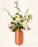 I en ferskenfarvet keramikvase er en buket af lyserøde og hvide kunstige silkeblomster, "Dreamy Meadow"-buketten, med grønne blade og stilke, mod en almindelig, lys baggrund.