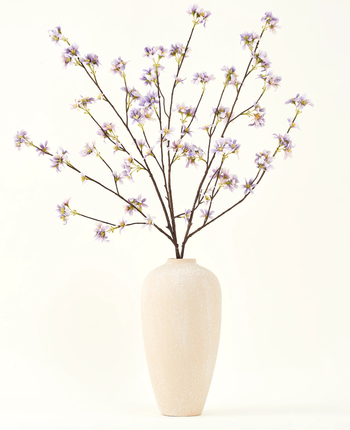 En høj, cremefarvet keramikvase indeholder en række tynde grene med teksten Silke kunstig blomsterbuket Kunstig blomstergren lilla, mod en almindelig, lys baggrund.