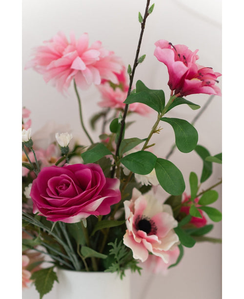 Et nærbillede af Artificial Rose Real Touch 56 cm pink, en buket lyserøde kunstige roser med grønne blade i en hvid vase, mod en lys baggrund.