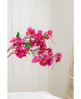 De Kunstbloem Bougainvillea 90 cm paars, met levendige paarse bloemen en groene bladeren, wordt getoond tegen een lichte neutrale achtergrond naast een houten ladder aan de rechterkant.