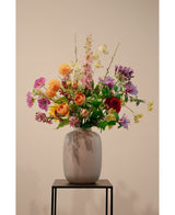 The Artificial Dogwood Real Touch Light Yellow 74cm, en naturtro lysegul kunstig blomst, står i en keramisk vase med grønt løv på et sort metalstativ mod en almindelig beige baggrund.