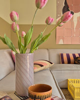 En 63 cm kunstig blomst fransk tulipan i pink står i en vase på bordet ved siden af ​​en orange kop i en hyggelig stue med creme sofa, mønstrede puder, en gul kasse og abstrakt vægkunst i baggrunden.