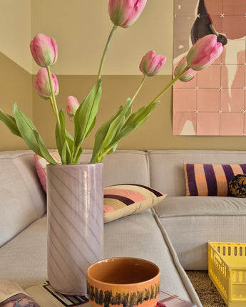 En 63 cm kunstig blomst fransk tulipan i pink står i en vase på bordet ved siden af ​​en orange kop i en hyggelig stue med creme sofa, mønstrede puder, en gul kasse og abstrakt vægkunst i baggrunden.