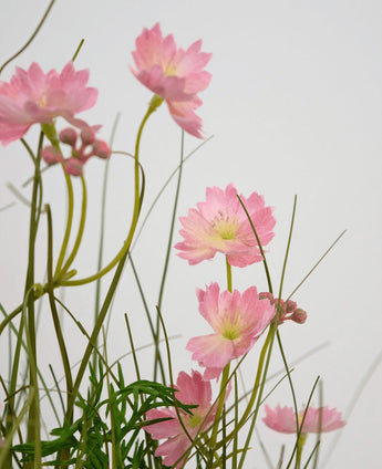 Artificial Grass Pink Gesang Flower Onion Grass Pot 56cm Brandhæmmende har sarte lyserøde blomster med slanke grønne stængler og smalle blade, arrangeret mod en lys baggrund for en blød, luftig effekt.