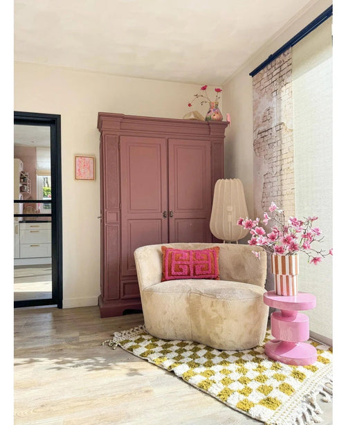En hyggelig læsekrog har en cremefarvet stol, lyserøde puder, et gult mønstret tæppe og en lilla garderobe. The Artificial Branch Magnolia lilleblomstret 89 cm pink står på et pink sidebord, mens store vinduer fylder dette indbydende rum med blødt lys.